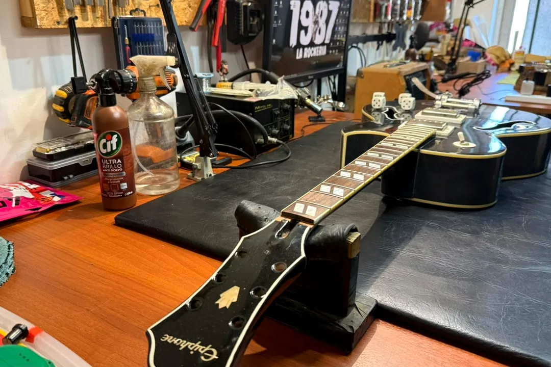 Guitarra acústica Epiphone apoyada en el banco de trabajo del taller, lista para ser intervenida