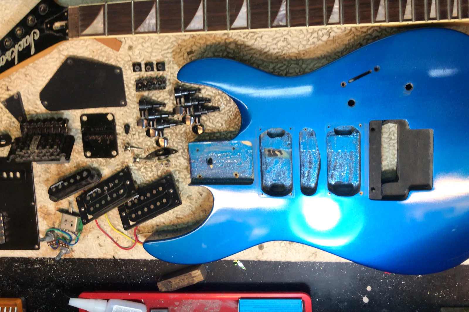 Guitarra eléctrica azul desarmada por completo, con todas sus piezas ordenadas sobre el banco