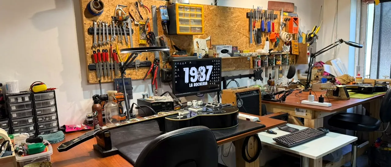 Banco de trabajo del taller de luthería de 1987 La Rockería, con la pared de herramientas y una guitarra acústica en reparación